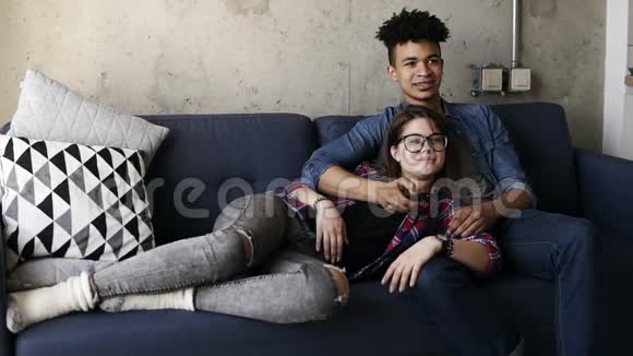 可爱的年轻夫妇在沙发上迷人的高加索女孩躺在她英俊的穆拉托男友的大腿上他在努力视频的预览图