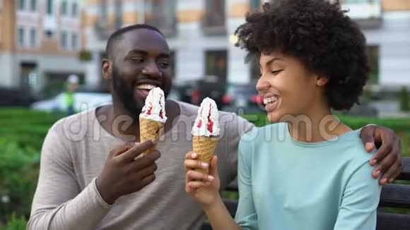 约会情侣吃冰淇淋坐在城市长椅上一起玩爱视频的预览图