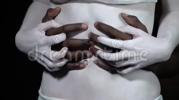 一个穿白色身体艺术的女孩把一个黑人的手推到她的腹部视频的预览图