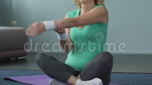 女性退休人员坐在健身垫上通过伸展手臂锻炼身体来热身视频的预览图