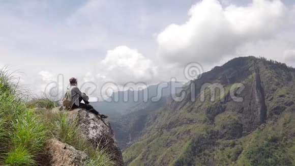 女旅行者坐在山上的大石头上视频的预览图