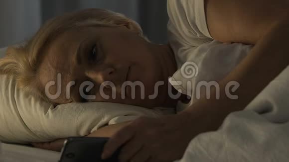 悲伤的养老女性在智能手机上聊天试图睡觉失眠视频的预览图