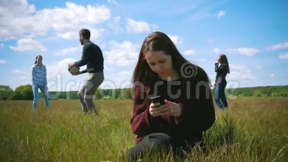 年轻女子坐在草地上背景是智能手机年轻朋友在夏天的场地上打排球视频的预览图