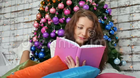 年轻的黑发正在阅读一本关于优雅圣诞树背景的书非常规色创意视频的预览图