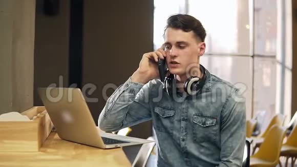 20穿着牛仔衬衫脖子上戴着无线耳机旁边放着笔记本电脑很有魅力的男性视频的预览图