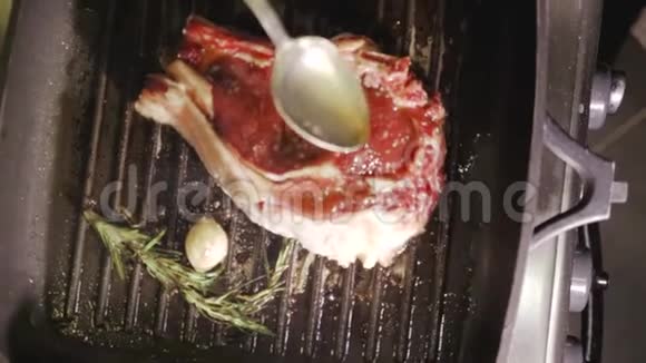 不可辨认的男厨师她用手在新鲜的牛肉牛排上倒油用迷迭香和大蒜在热黑色上烤视频的预览图