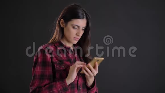 年轻美丽的白种人长发女孩在黑色背景下专注地观看智能手机的肖像视频的预览图