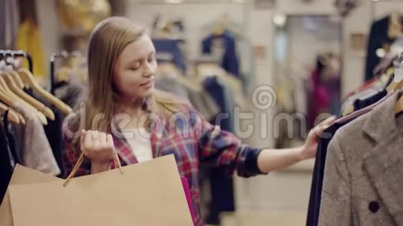 年轻漂亮的女购物者拿着购物袋在服装店里寻找新衣服视频的预览图