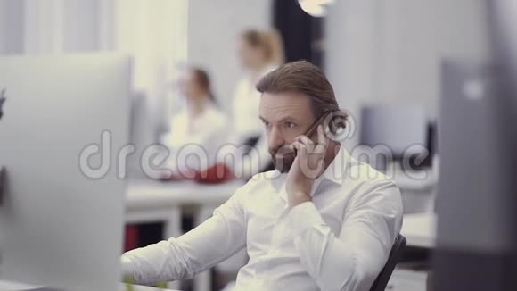 英俊的商人通过电话交谈在办公室的电脑工作视频的预览图