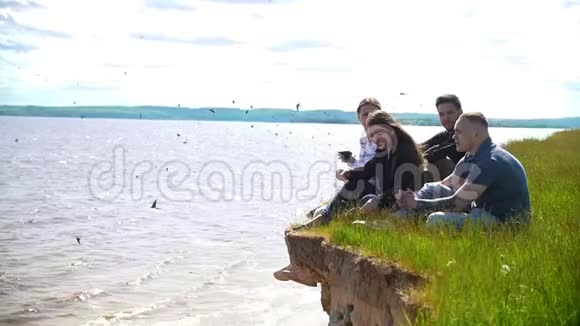 年轻的朋友坐在河边的山上享受大自然的周末视频的预览图