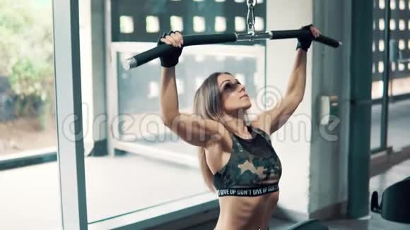 年轻健康女性在健身房用训练机做肩部运动的镜头视频的预览图