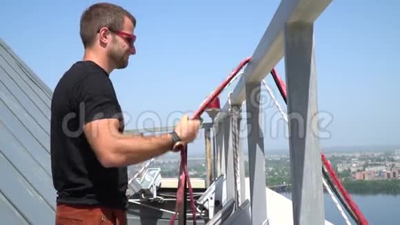 一个戴太阳镜的人站在大楼的屋顶上为松弛的绳索准备吊索视频的预览图