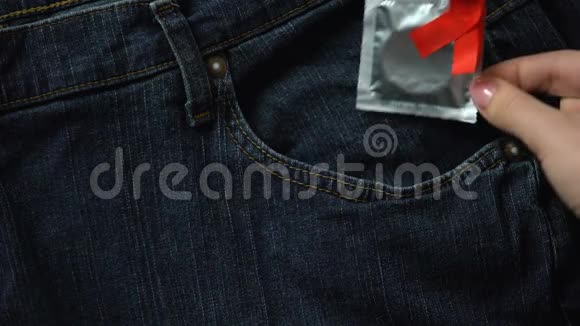 女士把带红丝带的避孕套放在牛仔裤口袋里安全性行为预防艾滋病视频的预览图
