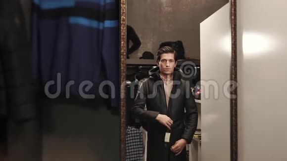 一个年轻人扣紧夹克对着一家服装店照镜子视频的预览图