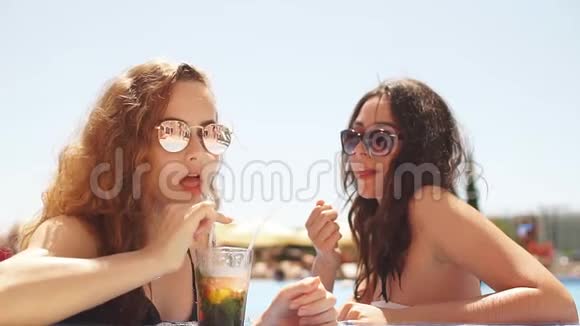 度假酒店的两位年轻女性正坐在泳池边清澈的海水旁度假视频的预览图