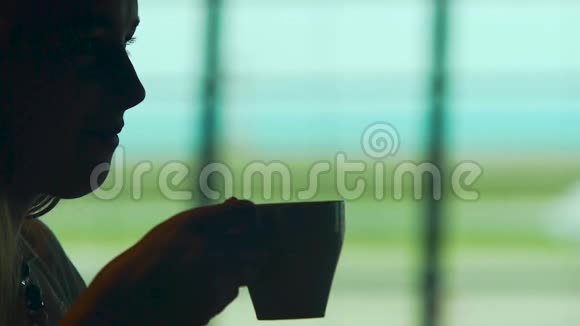 女主人坐在大窗户旁的咖啡厅喝咖啡等候机场视频的预览图