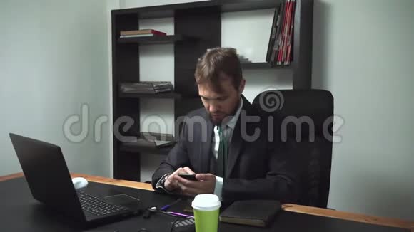 坐在笔记本电脑后面的办公室里一个穿着衣服的商人男工看着手机很生气很慢视频的预览图