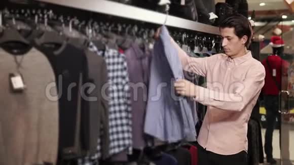 一个年轻人看衣架上的衣服他在服装店里挑选衬衫视频的预览图