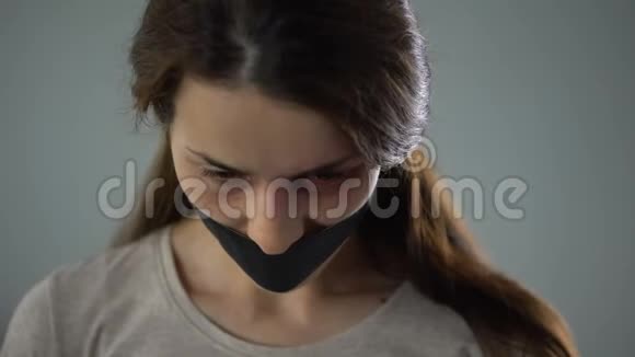 受伤的女人带着带子悲伤地看着镜头虐待的受害者视频的预览图