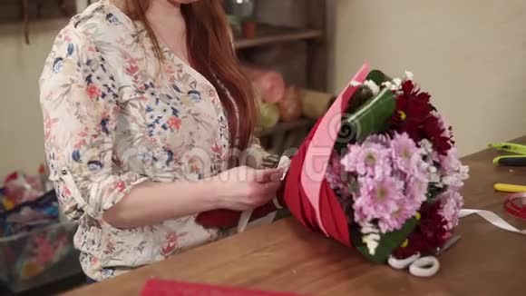 花女正在把白色的蝴蝶结绑在一束用红纸包裹的花上视频的预览图