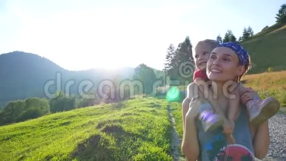 年轻女子展示她的女儿山妈妈把一个女儿扛在肩上沿着一条蜿蜒的山视频的预览图