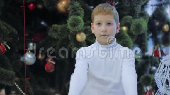 微笑的男孩展示了红色新年礼物小孩站在圣诞树下视频的预览图