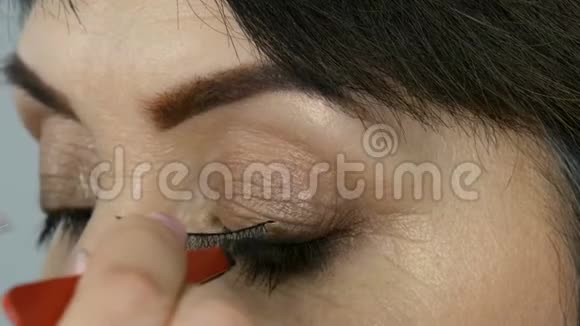 专业化妆师把假睫毛贴在一个成年中年妇女的蓝色眼睛上近距离观看视频的预览图