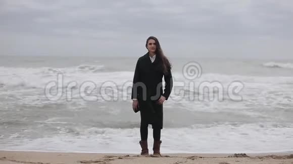一个美丽的女孩站在海滩上在寒冷的风日视频的预览图