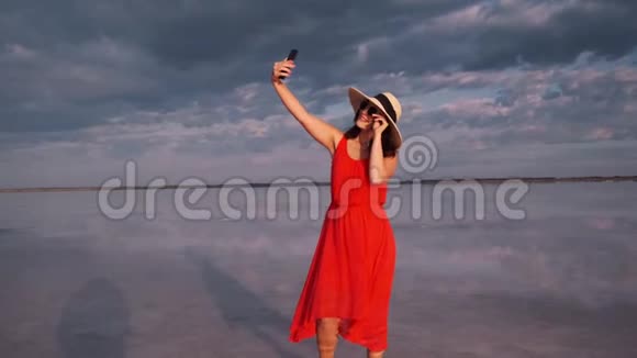 年轻的女人在一个美丽的不寻常的地方自拍穿着红色裙子帽子和太阳镜的女孩在粉红色的湖上视频的预览图