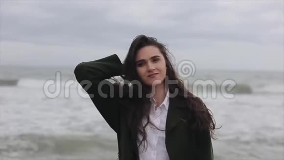 在寒冷的一天一个美丽的女孩站在大海的背景下抚摸着她宽松的长发很接近视频的预览图