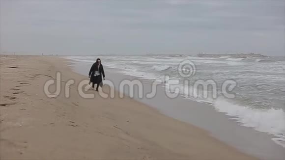 一个美丽的女孩在凉爽的春天沿着沙滩奔跑视频的预览图