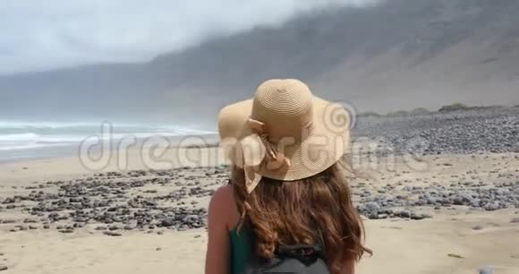 年轻女子带着草帽在卡拉塔法玛拉海滩漫步望着大海兰萨罗特视频的预览图