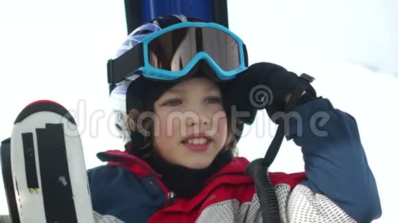 近距离拍摄戴着头盔和护目镜的少年男孩站在滑雪缆车舱里孩子开心地笑了有趣的假期视频的预览图