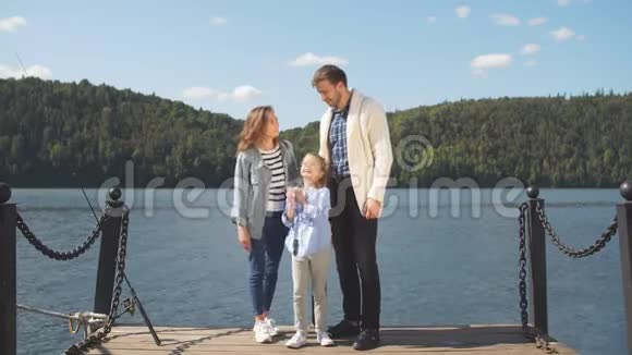 幸福的一家人在安静的湖边摆姿势时看着摄像机视频的预览图
