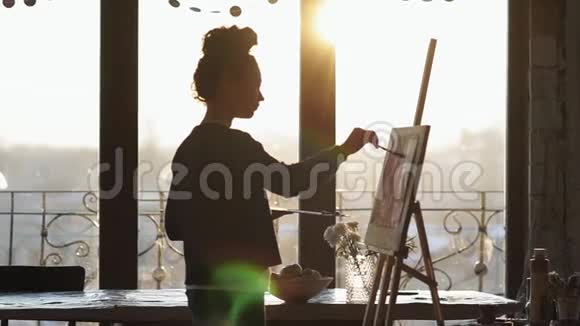 不可辨认的女性艺术家在画架上画在一个艺术工作室与全景窗口慢动作视频的预览图