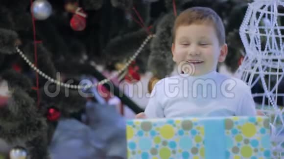 快乐男孩展示新年礼物小孩站在圣诞树下视频的预览图