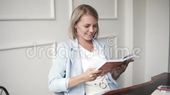 美丽而年轻的成功商务女性微笑着在咖啡馆里看书蓝色的金发女郎视频的预览图