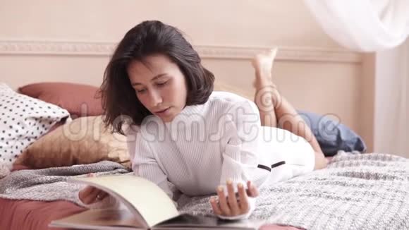 自信赤脚的女人躺在卧室里看杂志视频的预览图