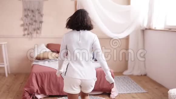 快乐的年轻女子在家里跳在床上做一个翻滚装饰室前段录像视频的预览图