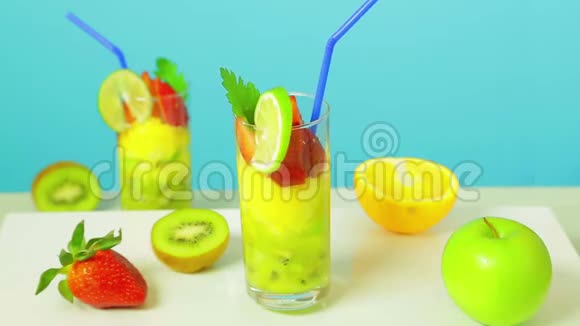 在一杯猕猴桃苹果和草莓切片中加入蓝色稻草装饰的水果鸡尾酒视频的预览图