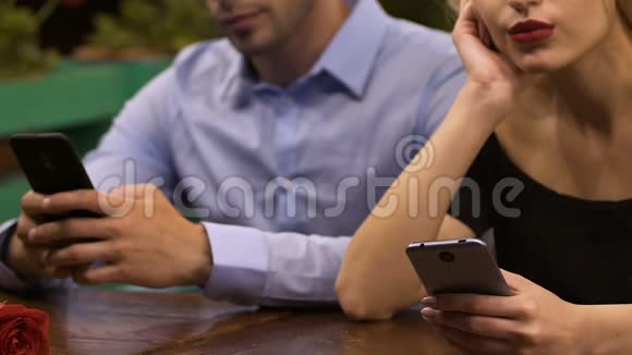一对年轻夫妇坐在桌子旁全神贯注地玩手机网络成瘾视频的预览图