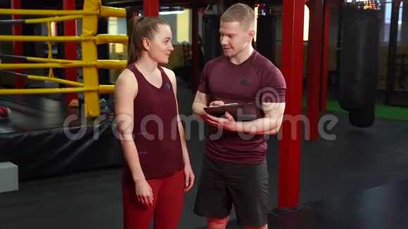 肌肉私人教练和年轻女子在健身房讨论训练计划视频的预览图