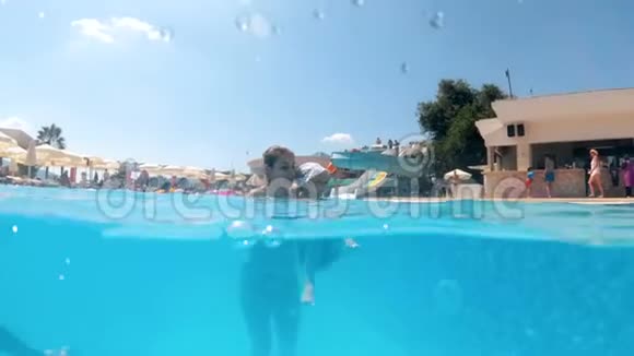 在酒店度假胜地的游泳池里年轻微笑的女人和她的小儿子一起游泳的慢镜头视频的预览图