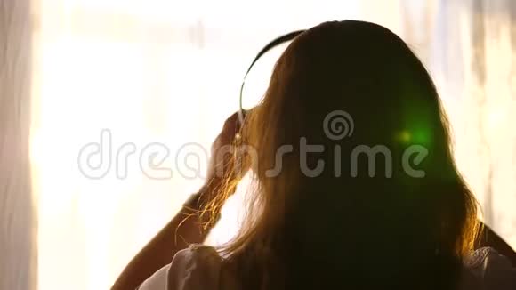 一个年轻的女孩来到窗口戴上耳机听音乐戴着耳机欣赏音乐的女人视频的预览图