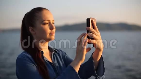 傍晚时分年轻美丽的高加索女人坐在海边的岩石上在她身上自拍视频的预览图