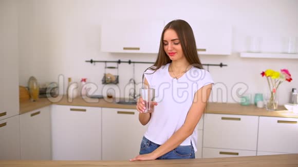年轻可爱的女孩从玻璃杯里喝净水皮肤的纯度一幅20多岁的白牙女士的阳光画像视频的预览图