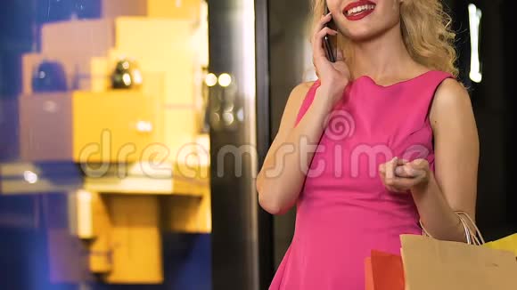年轻女子站在橱窗前拿着购物袋用手机说话视频的预览图