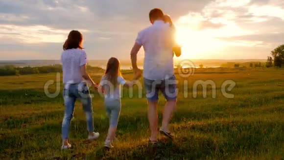 一个有孩子的家庭正沿着绿色的草地走向日落跑把孩子举起来拥抱爱视频的预览图