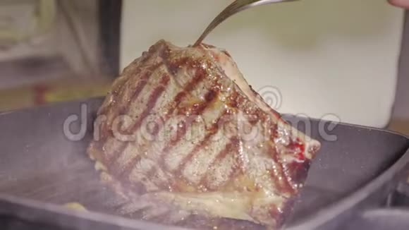 在热黑烤盘上烤一大块多多汁的牛排然后用人手中的勺子把油倒在上面视频的预览图