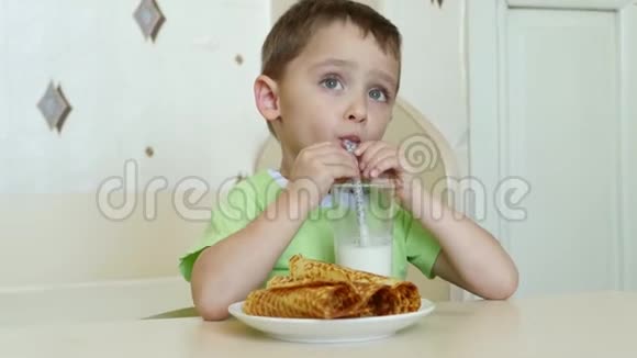一个快乐的孩子坐在桌边喝牛奶吃晶圆管视频的预览图